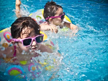 Two little girls swimming in a pool with goggles on.