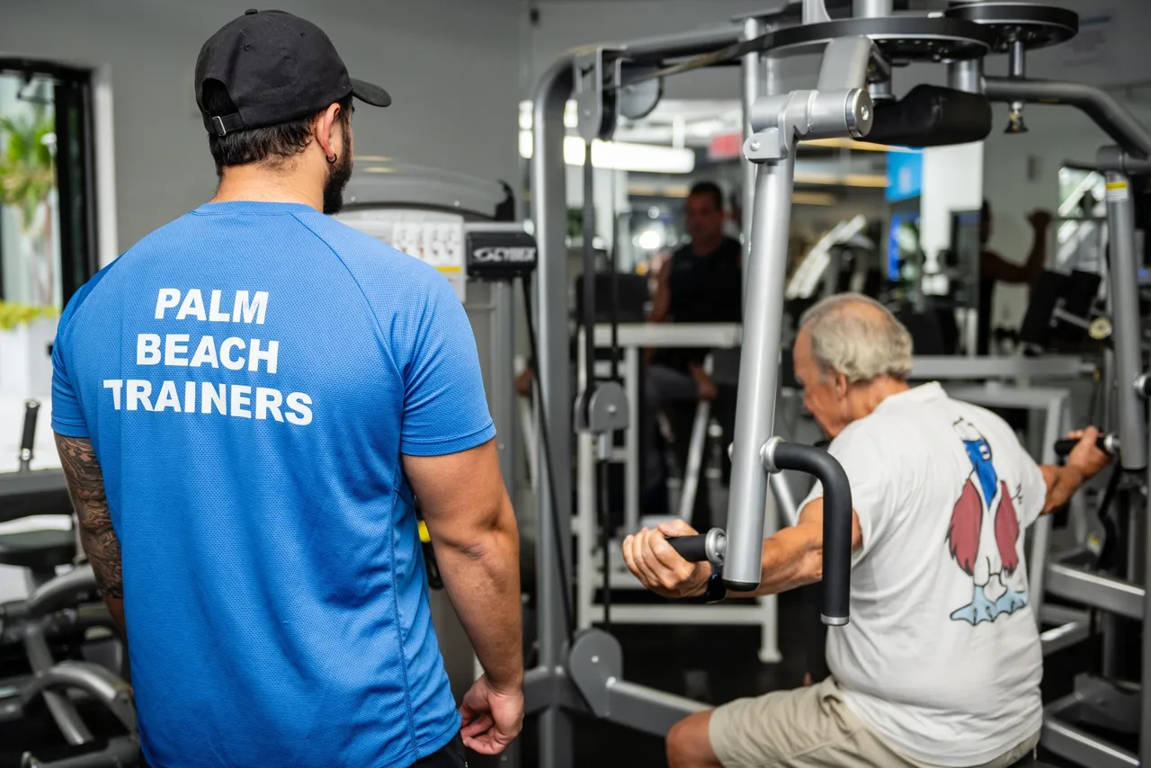 A man is working with an older person in the gym.