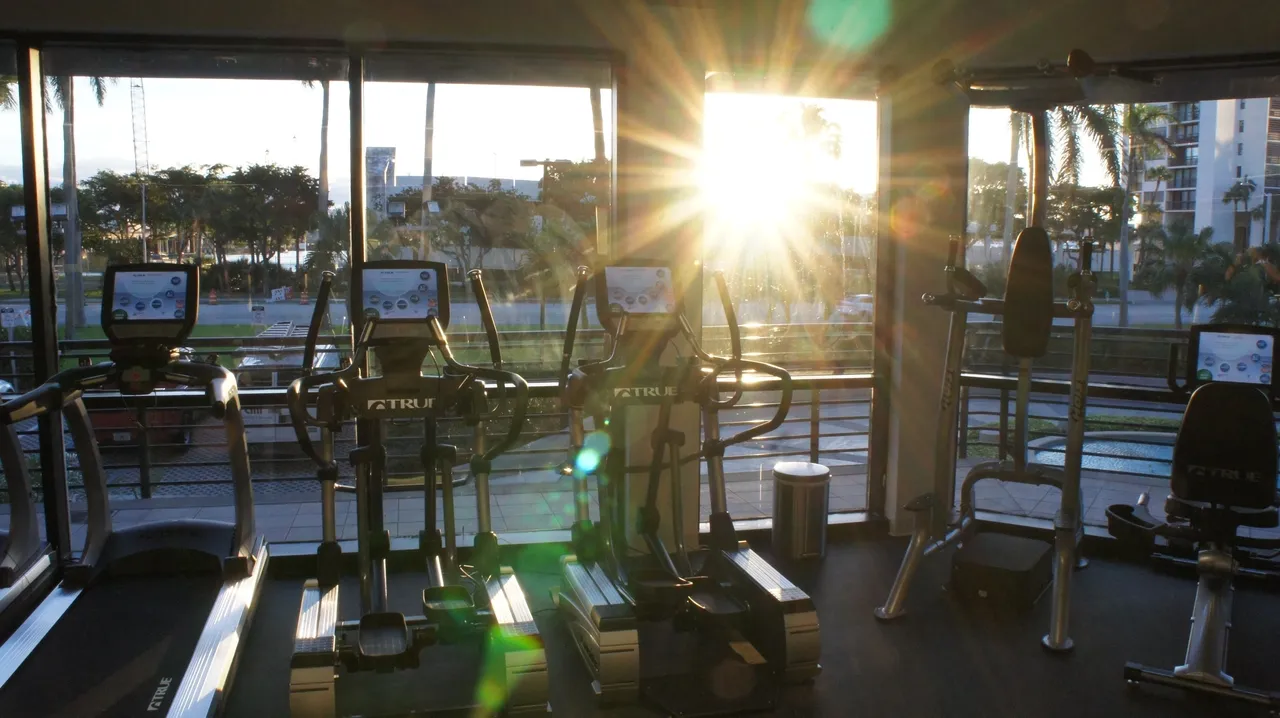 A gym with many machines and a sun setting.